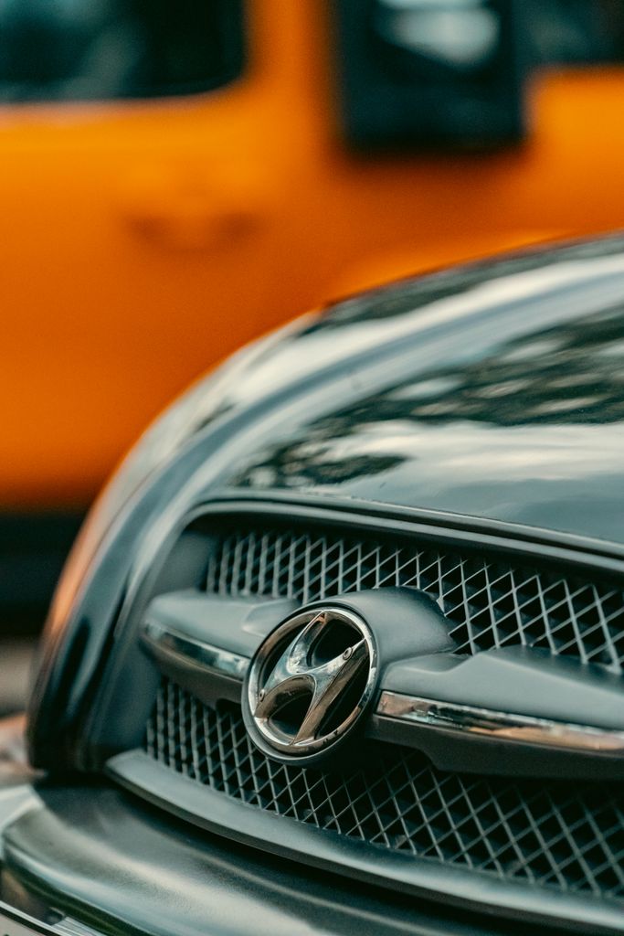Sharp image focusing on a car grille with a yellow vehicle in the background, capturing urban details.